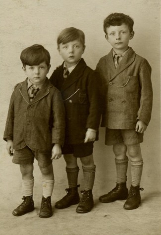 Photograph of three young boys, increasing in height from left to right.
			All are wearing suits with shorts, long socks and boots.
