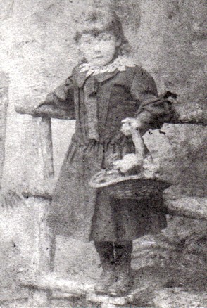 Grainy photograph of a young girl. She appears to be posed against a fence and is holding a basket of flowers.