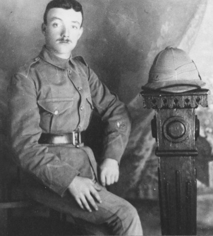 Very posed picture of a soldier in uniform.
				The man has very dark hair and is sporting a small moustache.
				This uniform bears no insignia.
				Beside him is a wooden stand topped with a pith helmet.