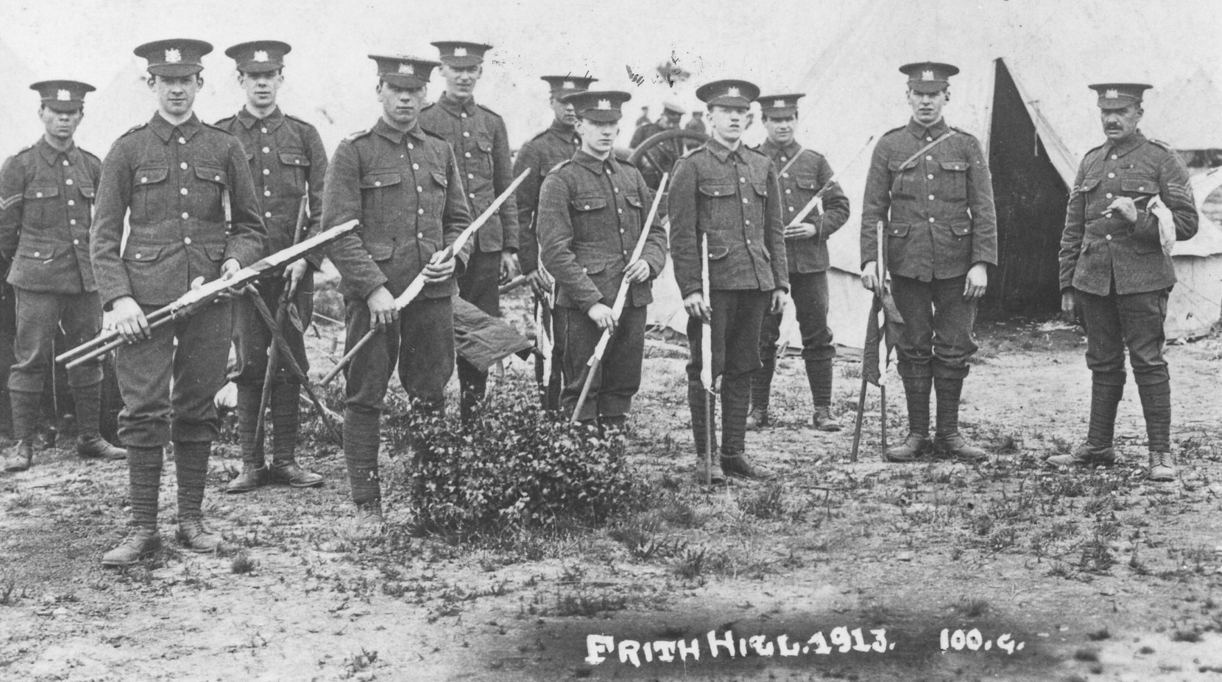 A group of soldiers all in quite smart uniforms.
					Some of them are holding rolled signal flags.
					On the far right appears to be an officer.
					Scratched on the bottom is the caption 'Frith Hill 1913'
